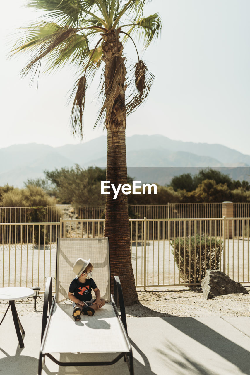 Young toddler boy with a mask on sitting by pool in palm springs