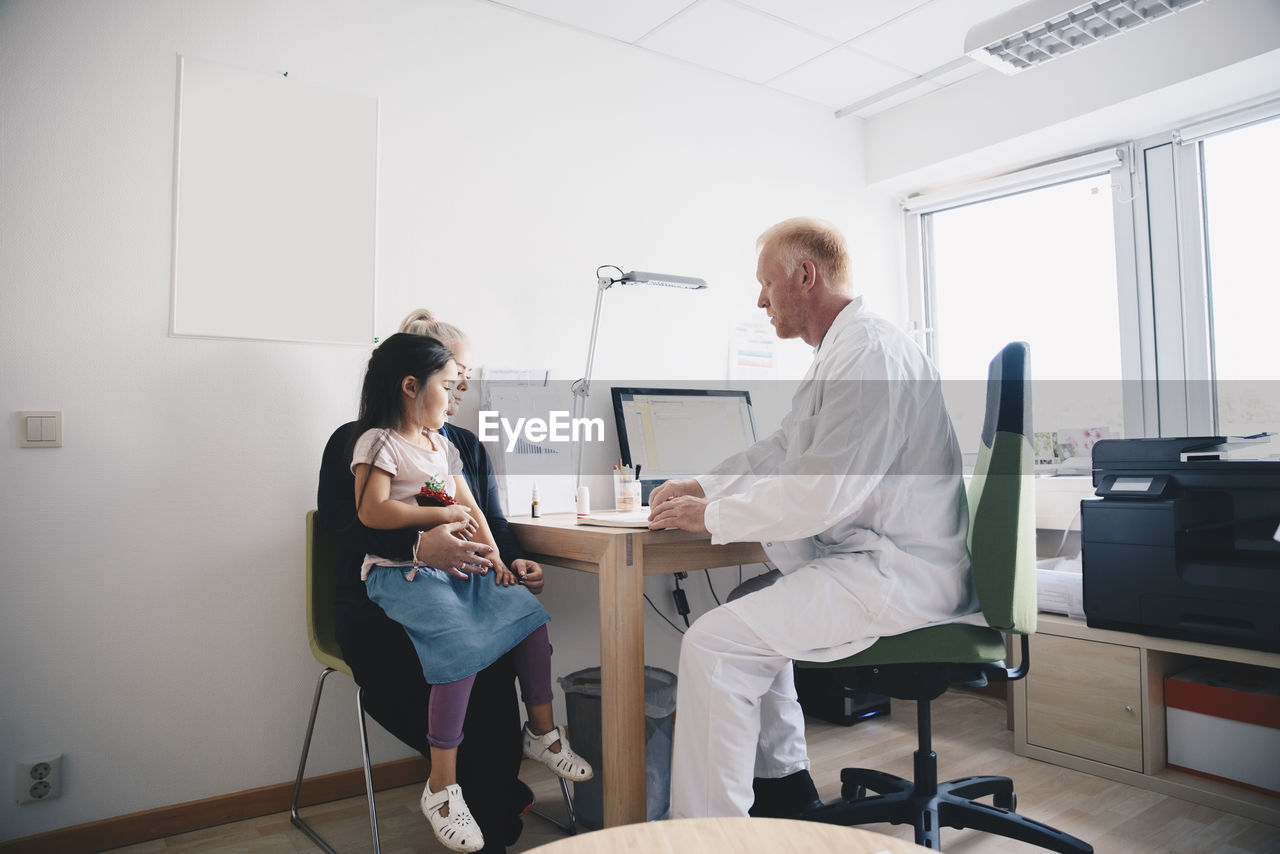 Mature doctor sitting with woman and girl in office at hospital