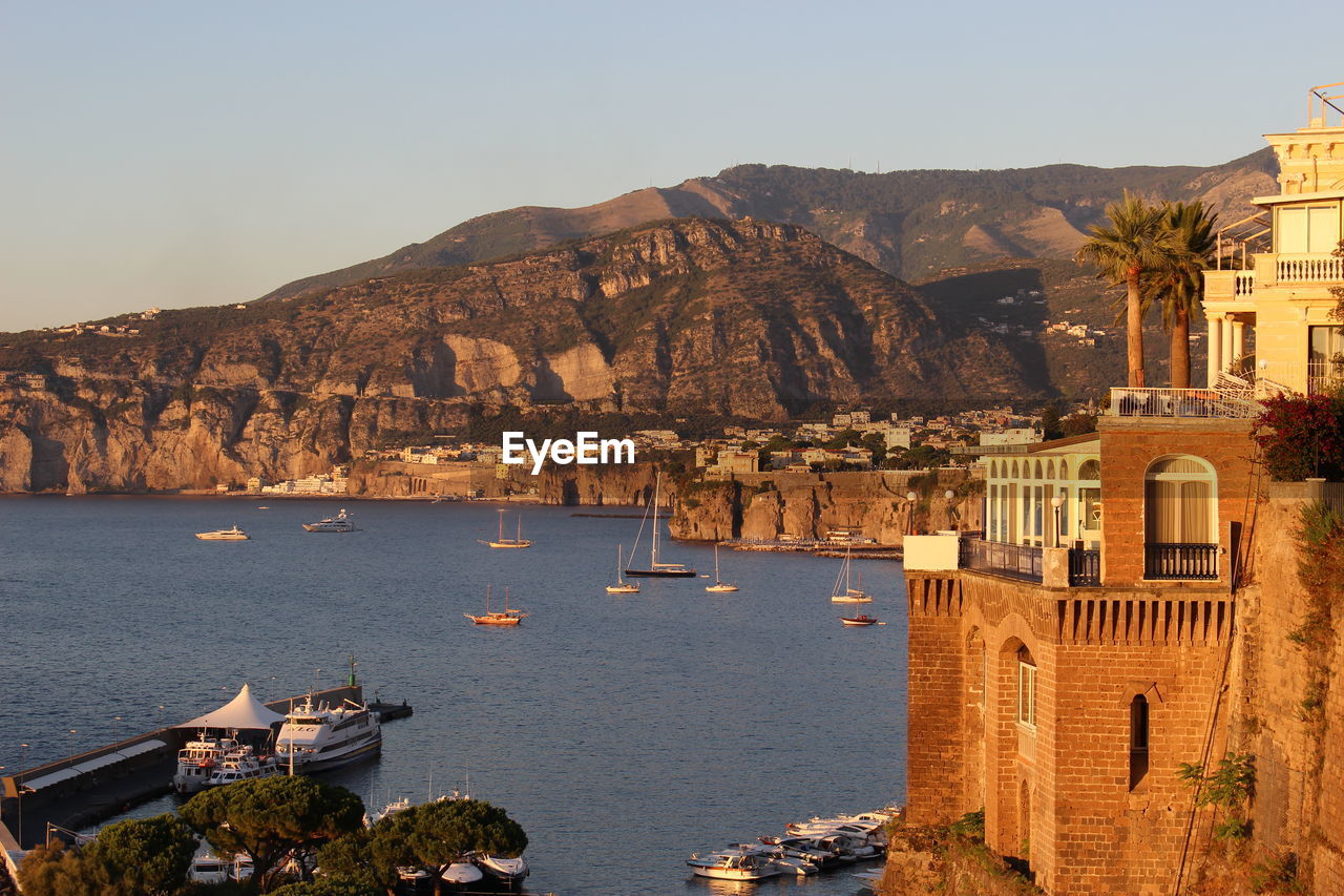 High angle view of boats moored at sea by historic building against mountains