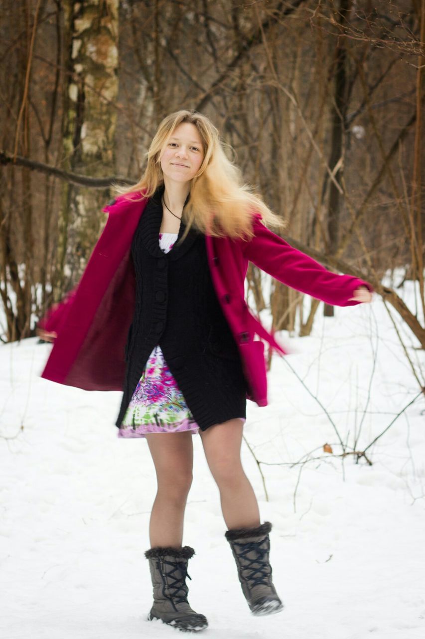 PORTRAIT OF A SMILING YOUNG WOMAN STANDING ON SNOW COVERED FIELD