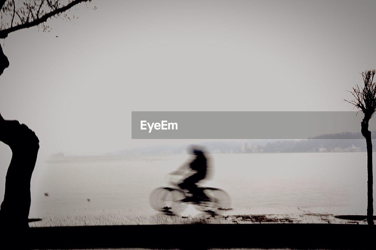 Defocused image of person riding bicycle by river against clear sky