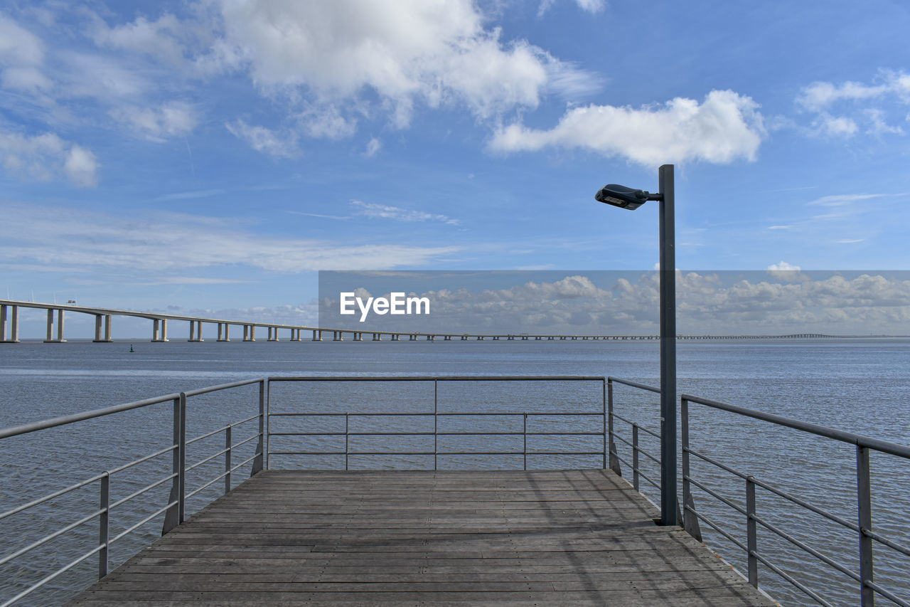 sky, walkway, water, cloud, railing, sea, pier, ocean, nature, coast, boardwalk, horizon, scenics - nature, beauty in nature, architecture, tranquility, tranquil scene, no people, day, outdoors, shore, travel destinations, horizon over water, built structure, beach, travel, blue, the way forward, transportation, land, tourism, street light, environment, idyllic, footpath, landscape, holiday, bridge, sunlight, city, wood, vacation, trip