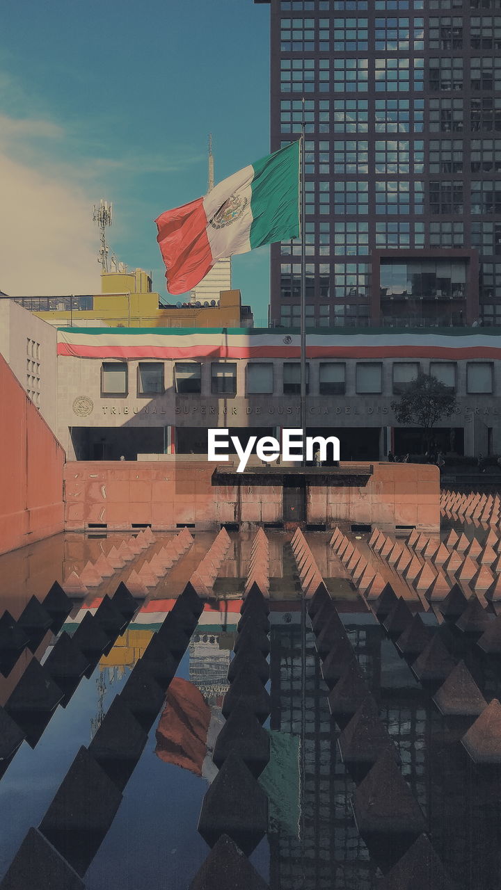 Reflection of mexican flag and buildings in pond