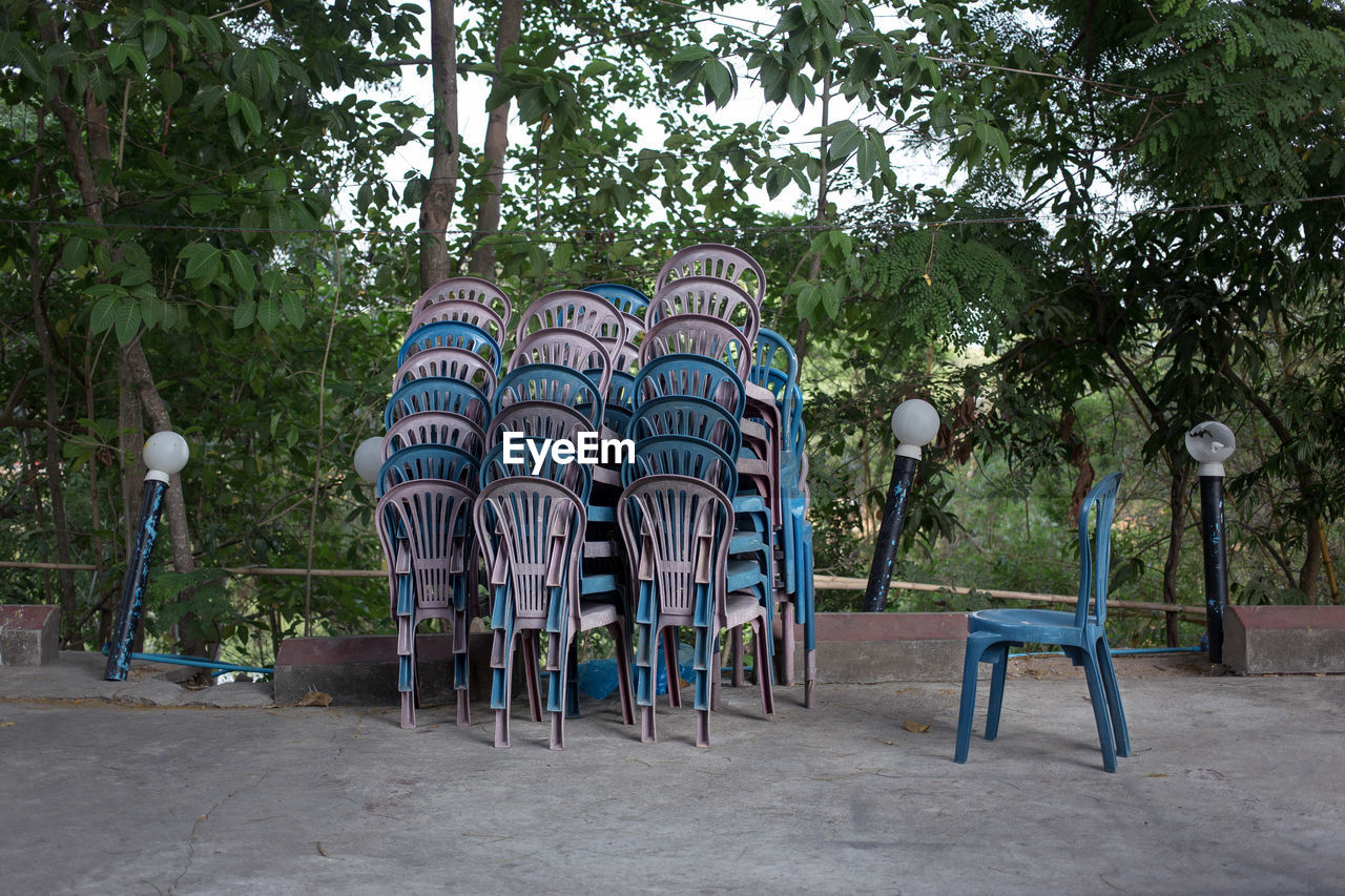Stack of chairs on footpath against trees
