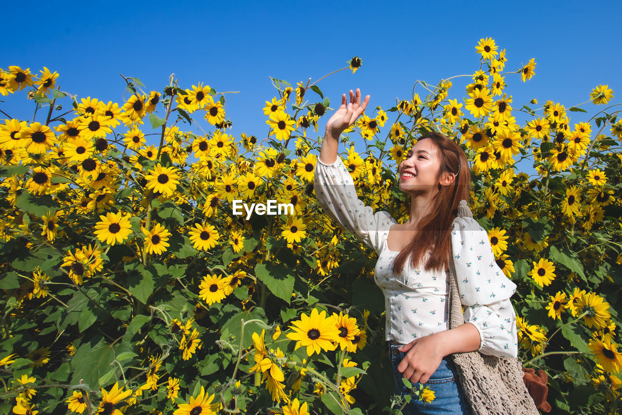 Young woman standing by yellow flowering plants