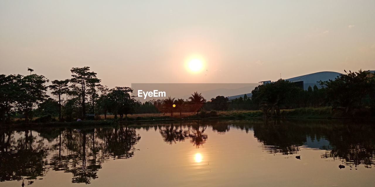 REFLECTION OF SILHOUETTE TREES ON LAKE AGAINST SKY DURING SUNSET