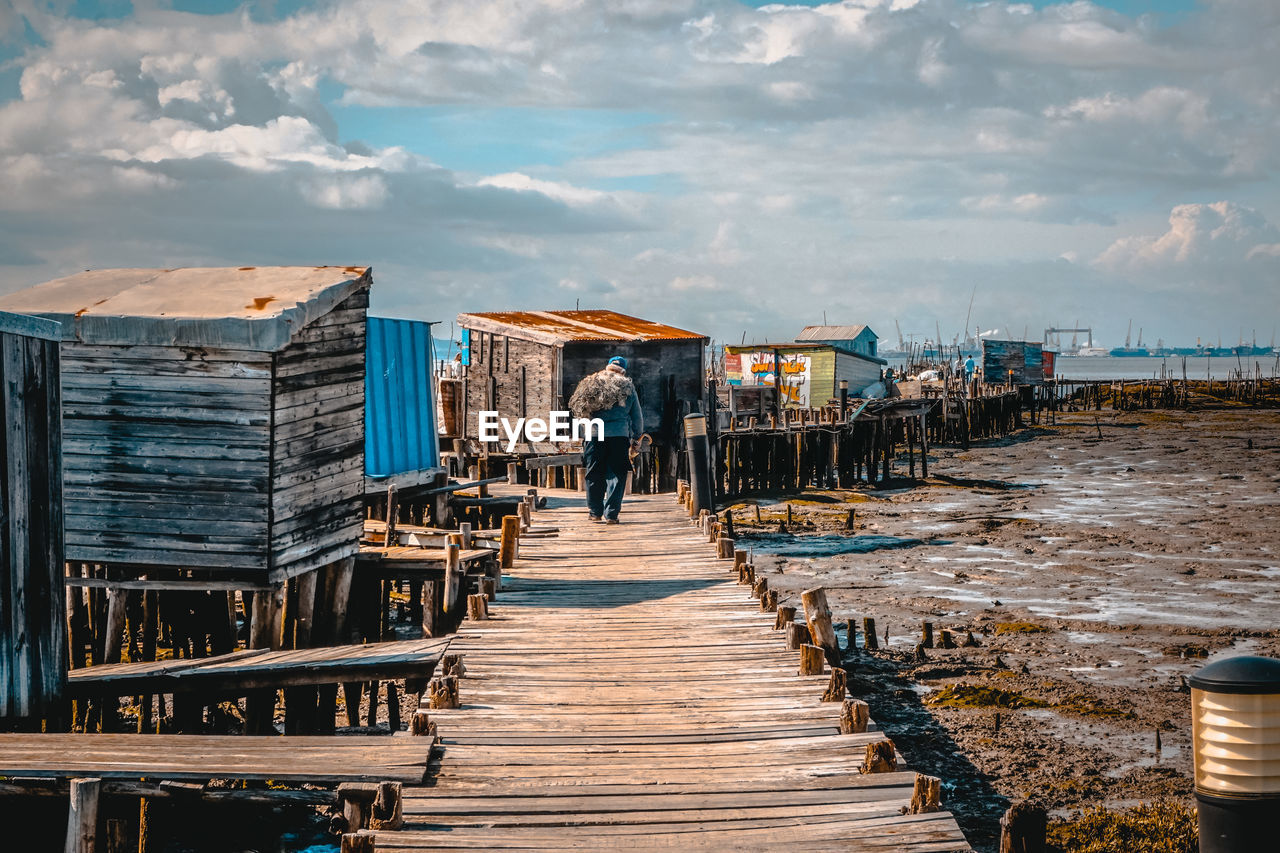 Rear view of man walking on pier at beach against sky