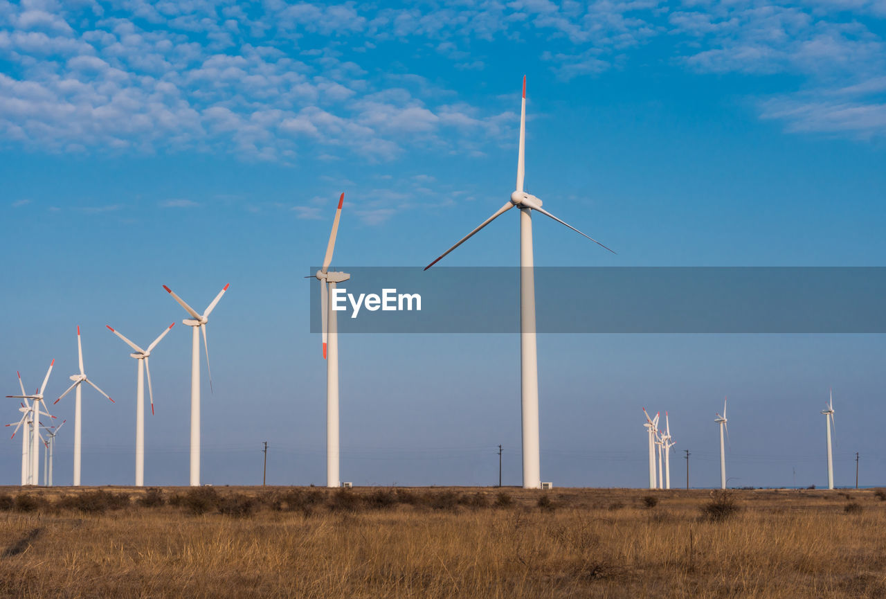 WINDMILLS ON FIELD AGAINST BLUE SKY