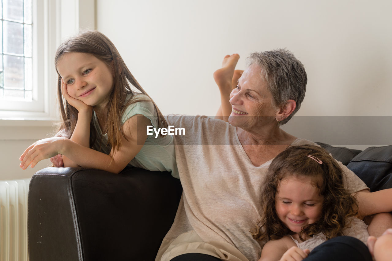 Smiling grandmother with granddaughters on sofa at home