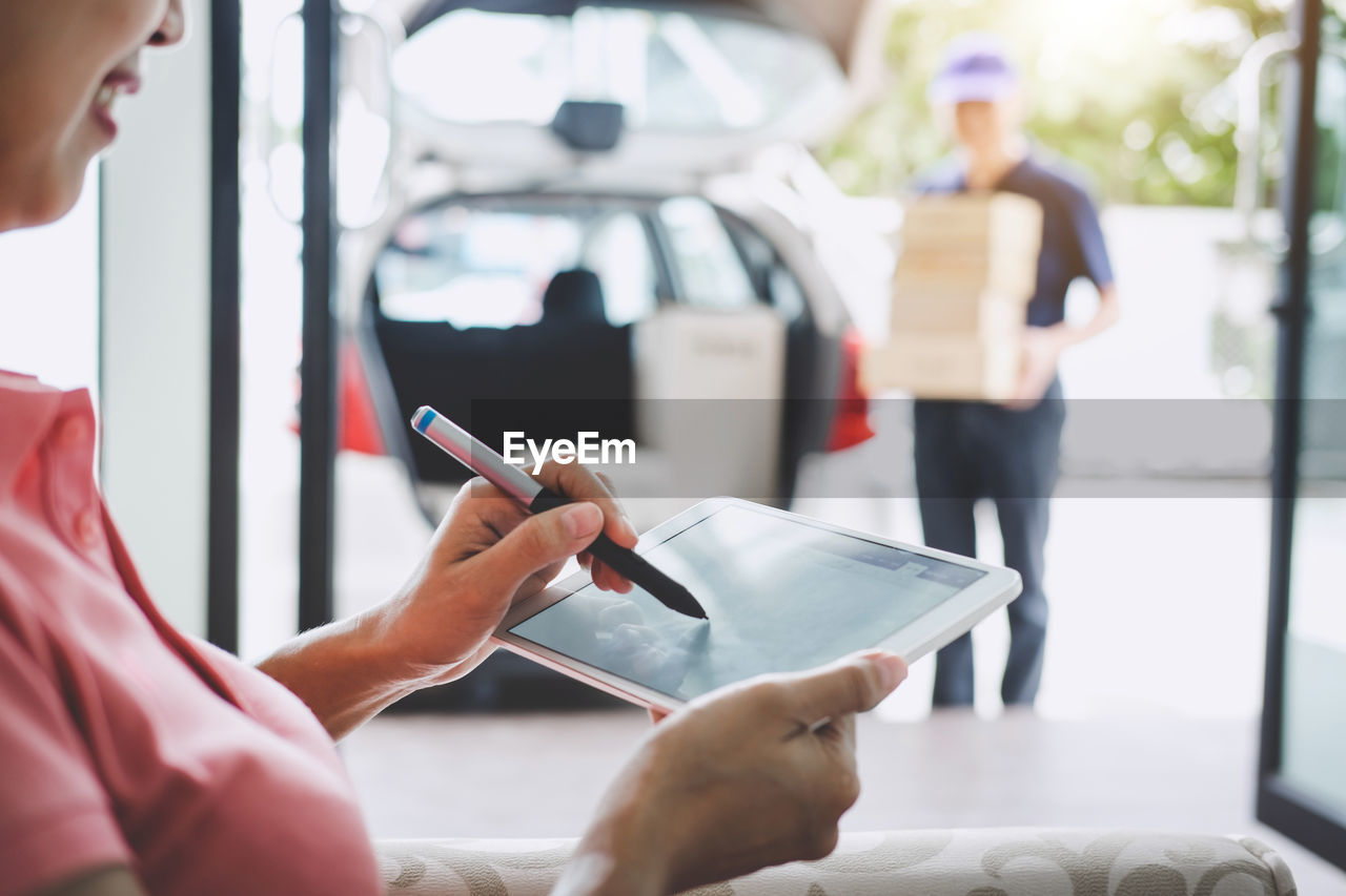 Midsection of woman signing on digital tablet while receiving delivery at home