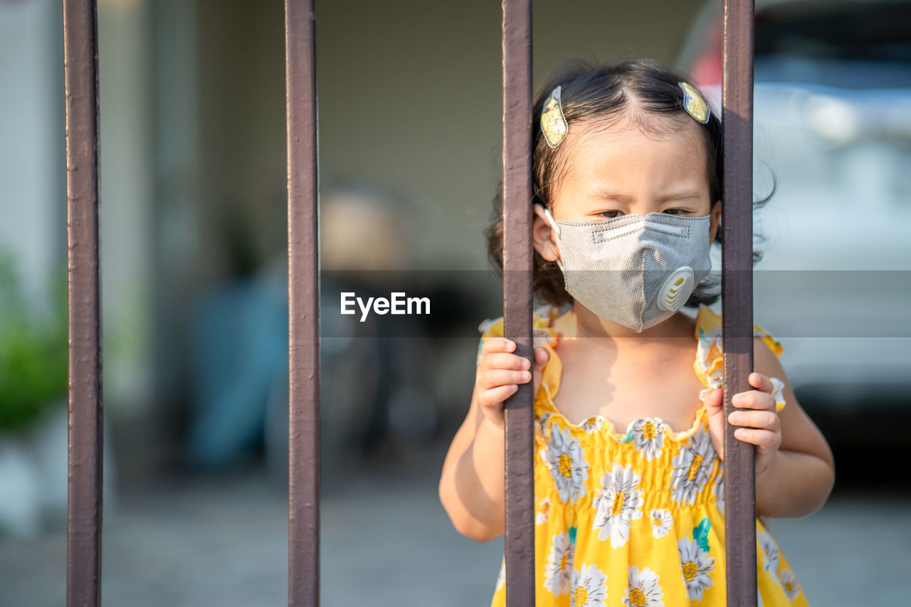 Girl standing at fence wearing medical face mask to prevent flu, pollution and covid 19.