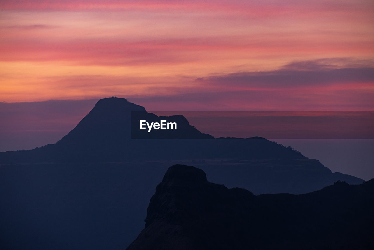 SCENIC VIEW OF SILHOUETTE MOUNTAINS AGAINST ORANGE SKY