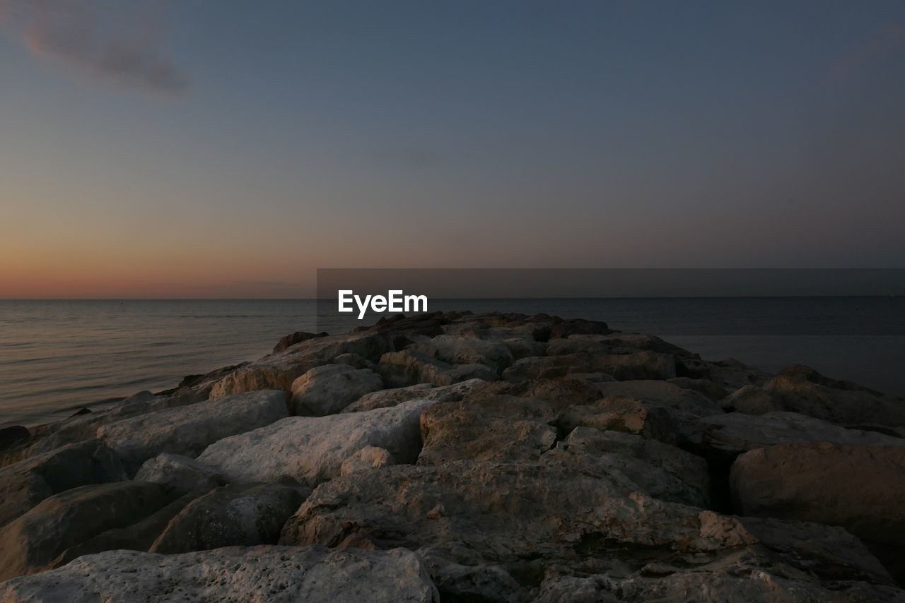 Rocks by sea against sky during sunset