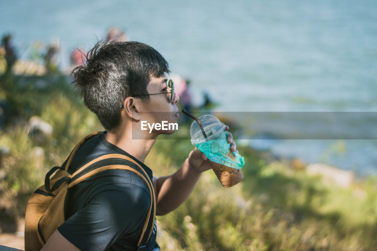 Young man having drink by sea