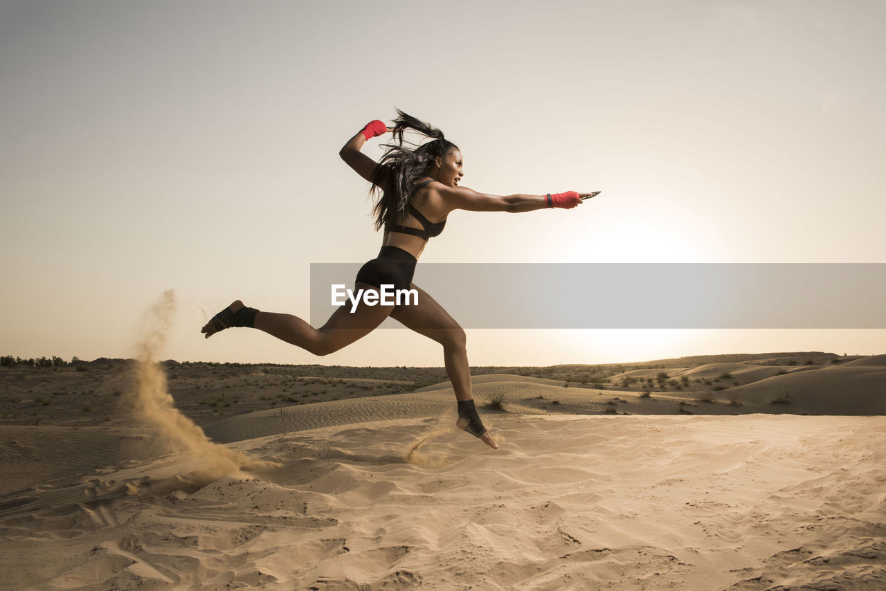 Woman jumping on desert against clear sky