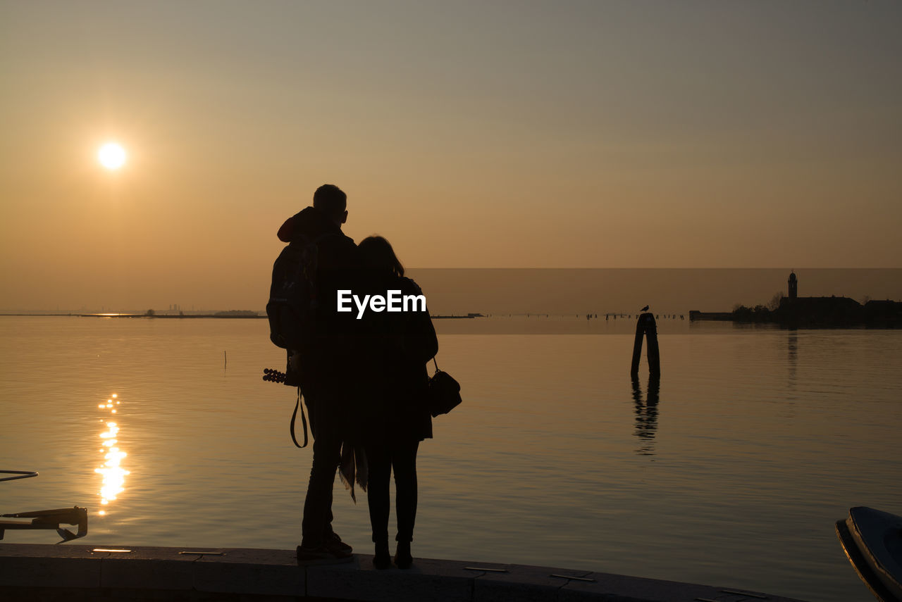 Silhouette people standing on beach against sky during sunset