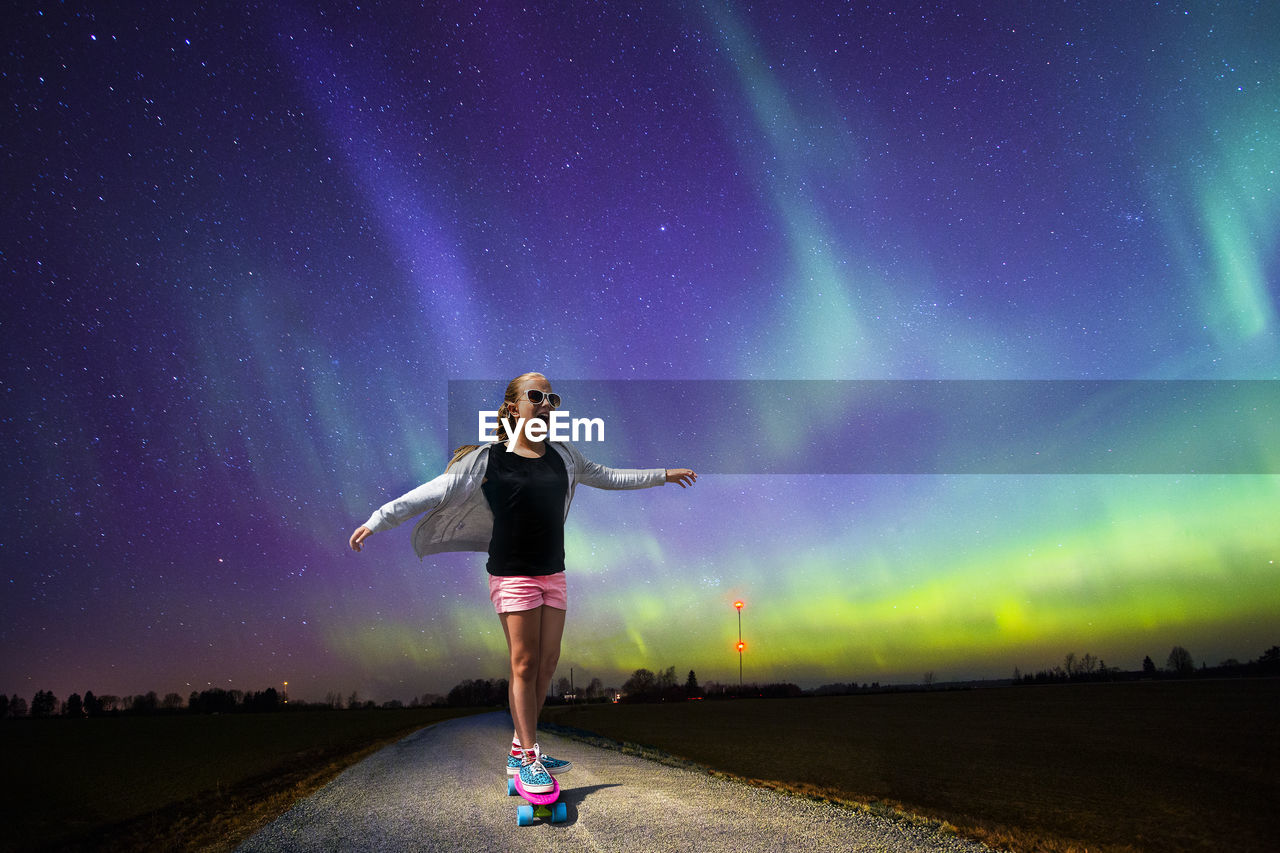 Girl skateboarding against star field at night