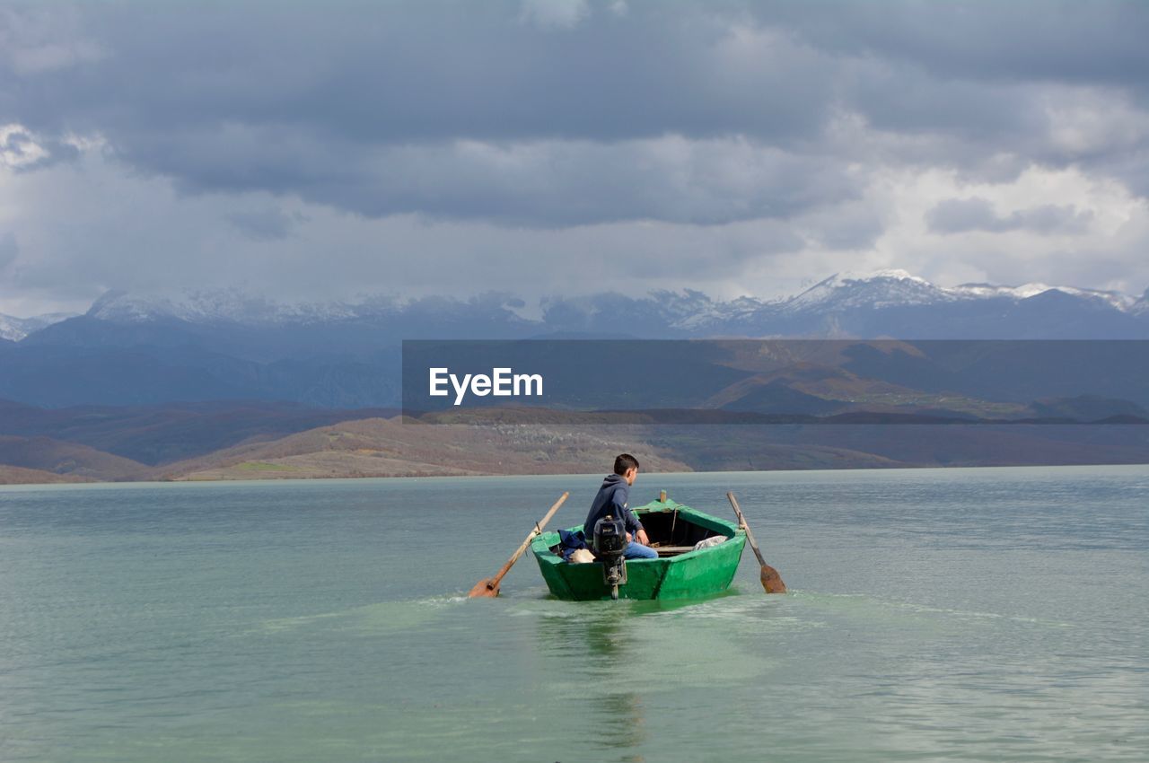 Man sailing boat in lake against mountains