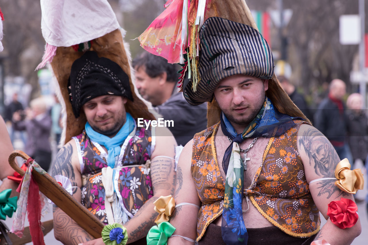 PORTRAIT OF FRIENDS STANDING AGAINST TRADITIONAL CLOTHING