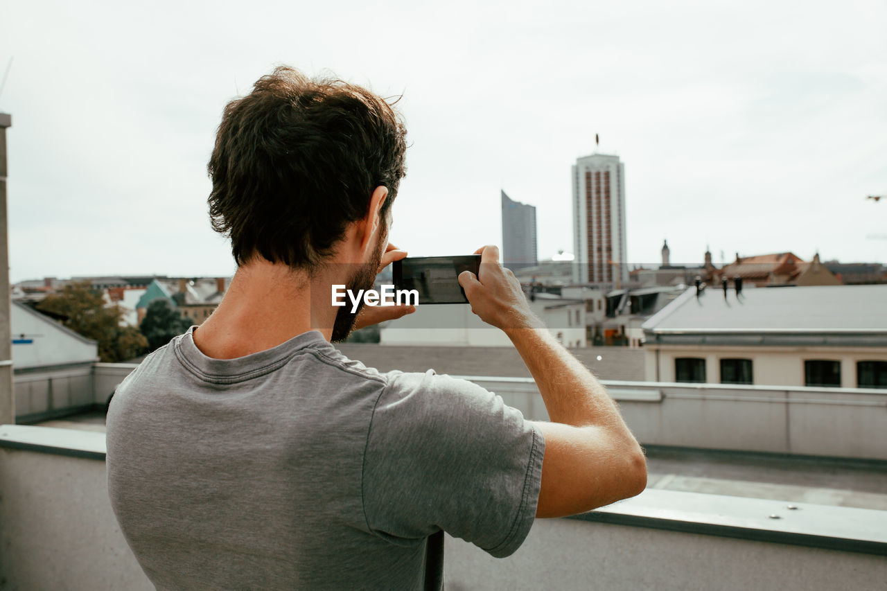 Rear view of man photographing city through mobile phone