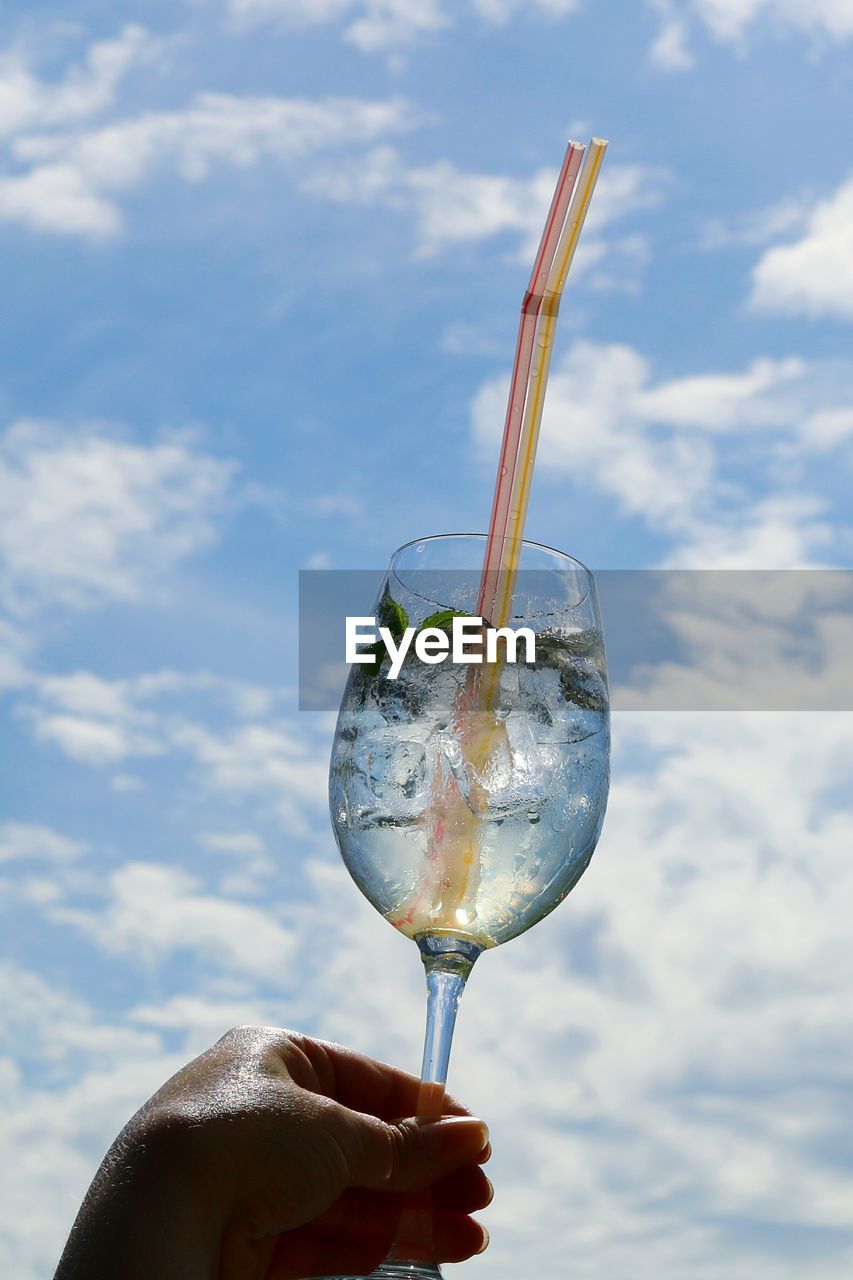 Cropped hand of woman holding wineglass against cloudy sky during sunny day