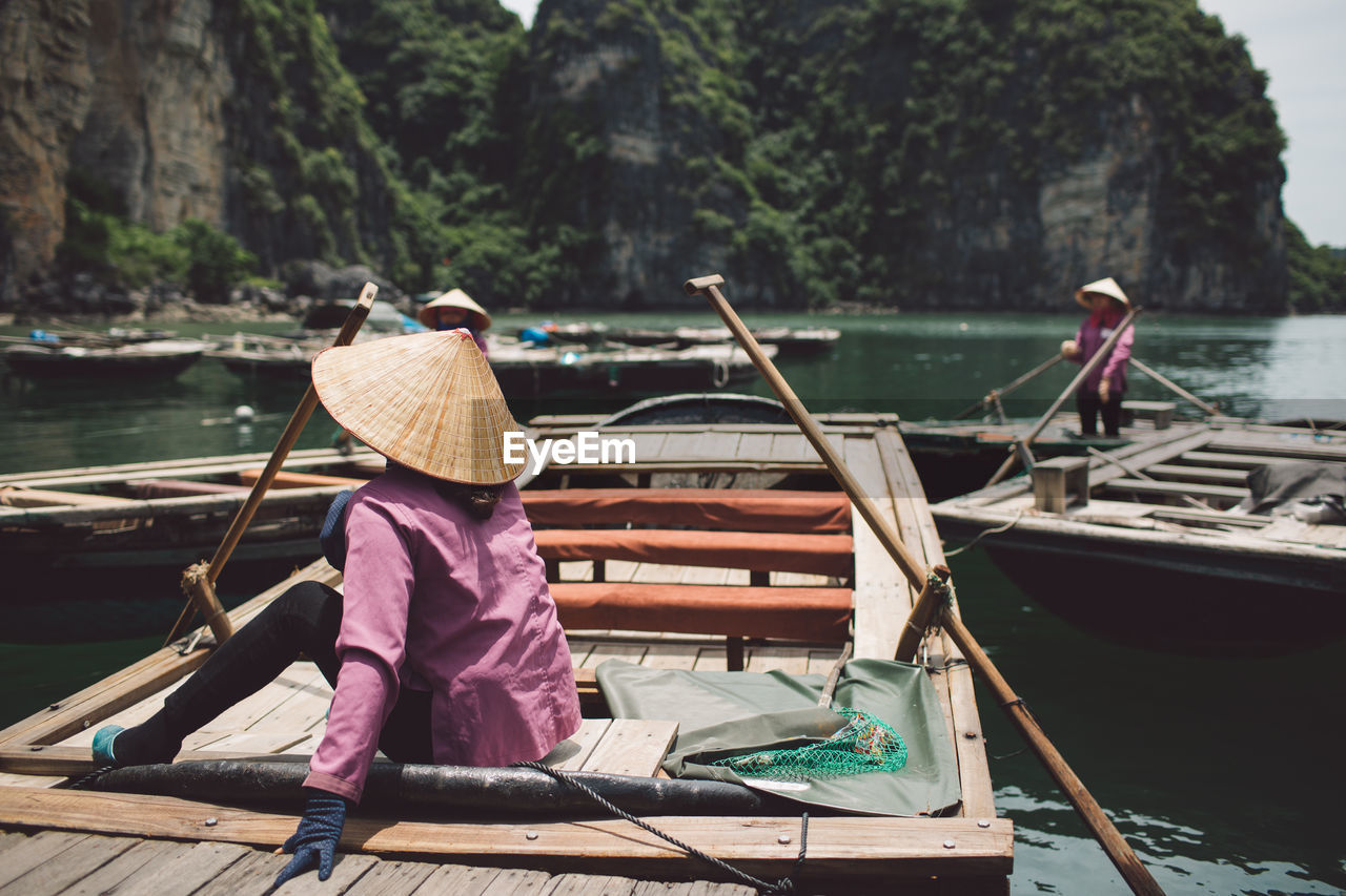 Rear view of woman wearing asian style conical hat while sitting on rowboat at halong bay