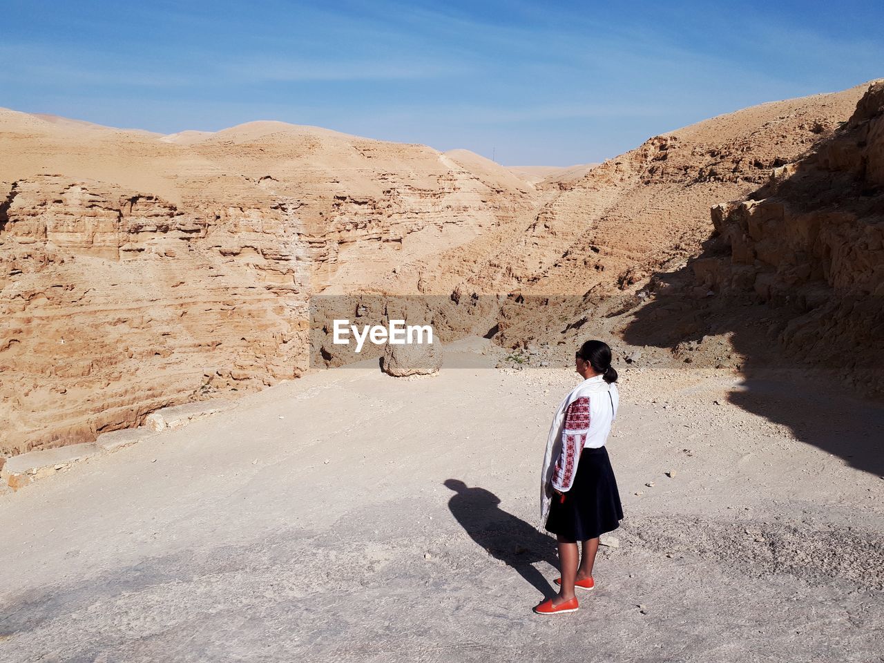 Rear view of woman standing by rock formation against sky