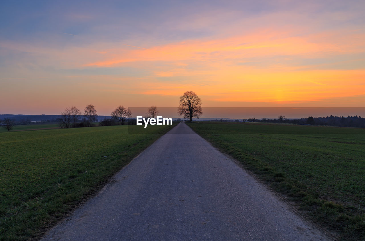 Road amidst field against sky during sunset