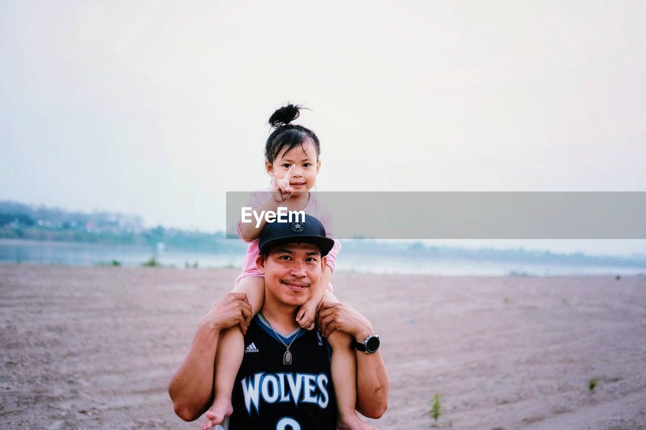 Family portrait of smiling young man and daughter on beach