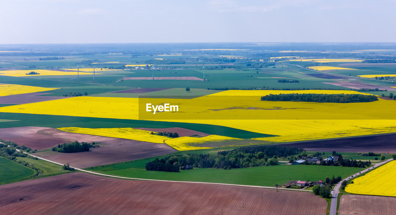 landscape, plain, environment, land, scenics - nature, field, horizon, nature, beauty in nature, rural scene, sky, tranquil scene, rapeseed, yellow, tranquility, aerial photography, aerial view, grassland, water, agriculture, day, plant, non-urban scene, no people, green, high angle view, idyllic, prairie, hill, farm, travel, transportation, outdoors, rural area, travel destinations, grass, cloud, sea, patchwork landscape, canola, horizon over land, remote