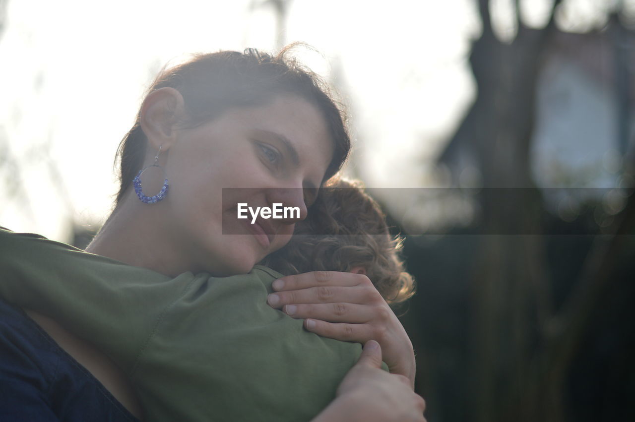 Happy mother holding little child in her arms with love in a garden outdoors in summertime
