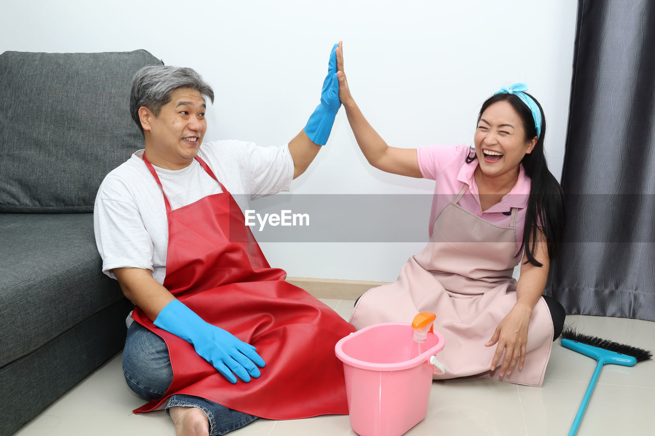 Full length of couple giving high five while sitting on floor at home