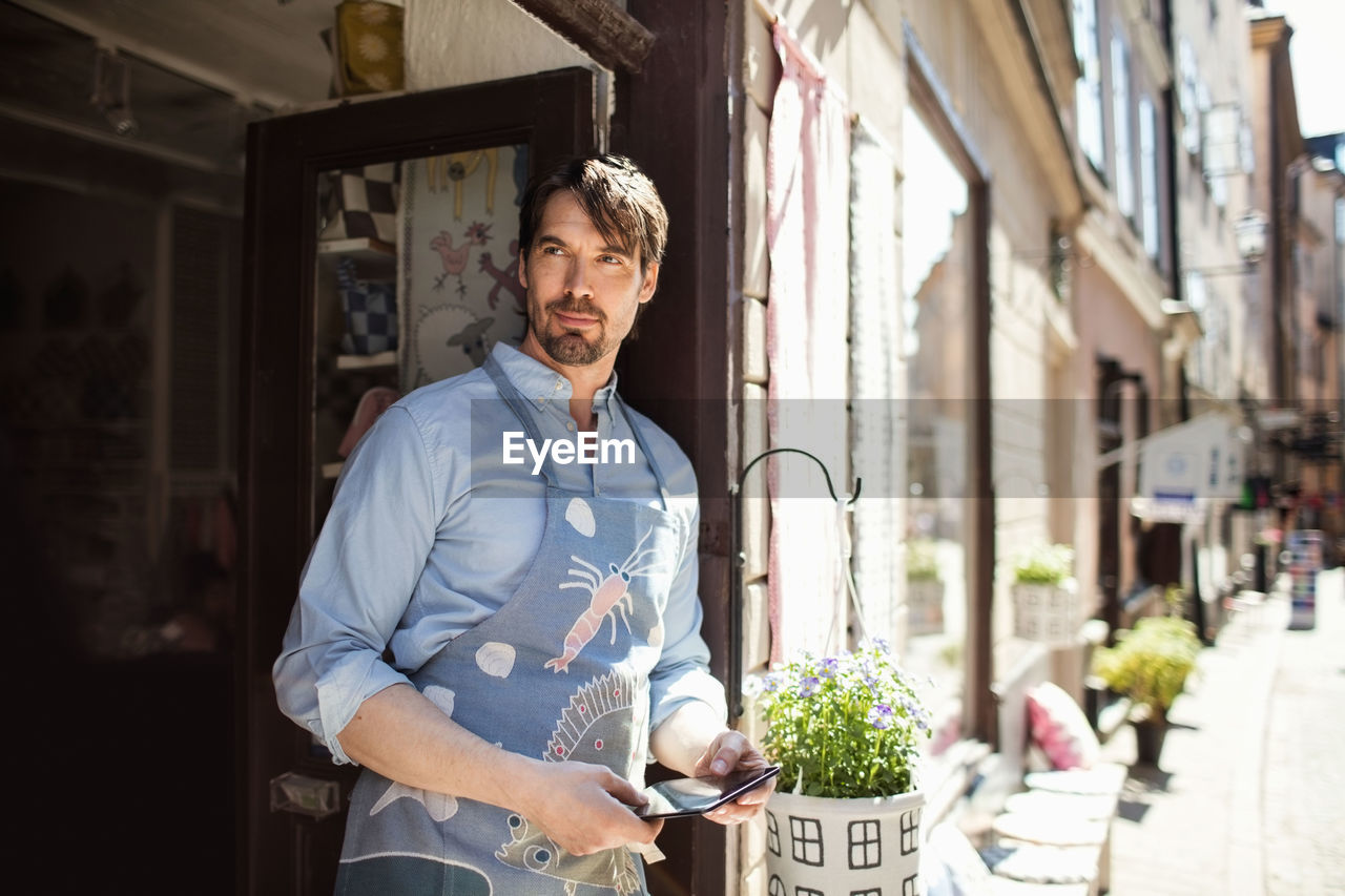 Confident owner holding digital tablet while standing at entrance of fabric shop