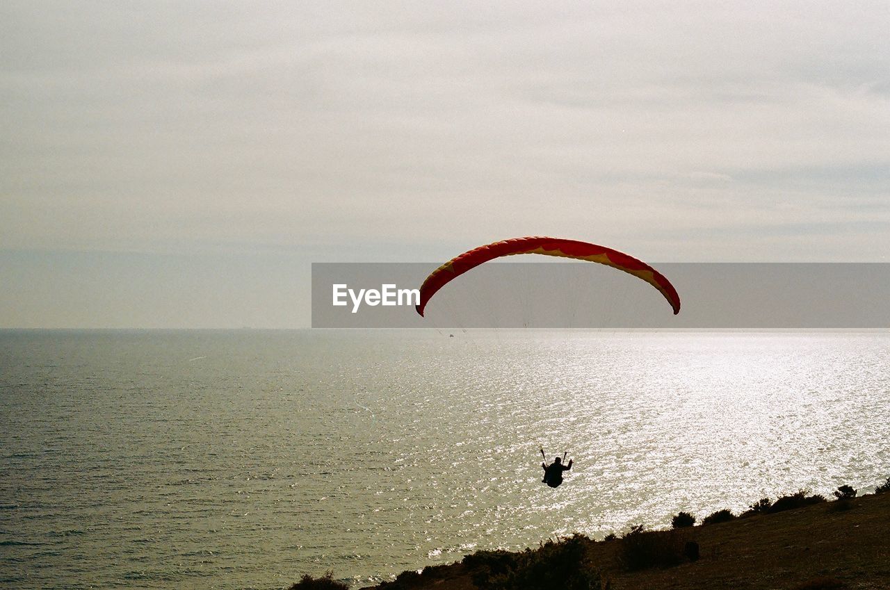 Silhouette person paragliding over sea against sky