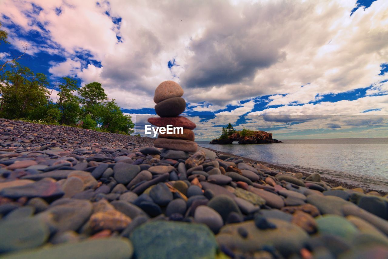 Surface level view of stones stacked at seashore against cloudy sky