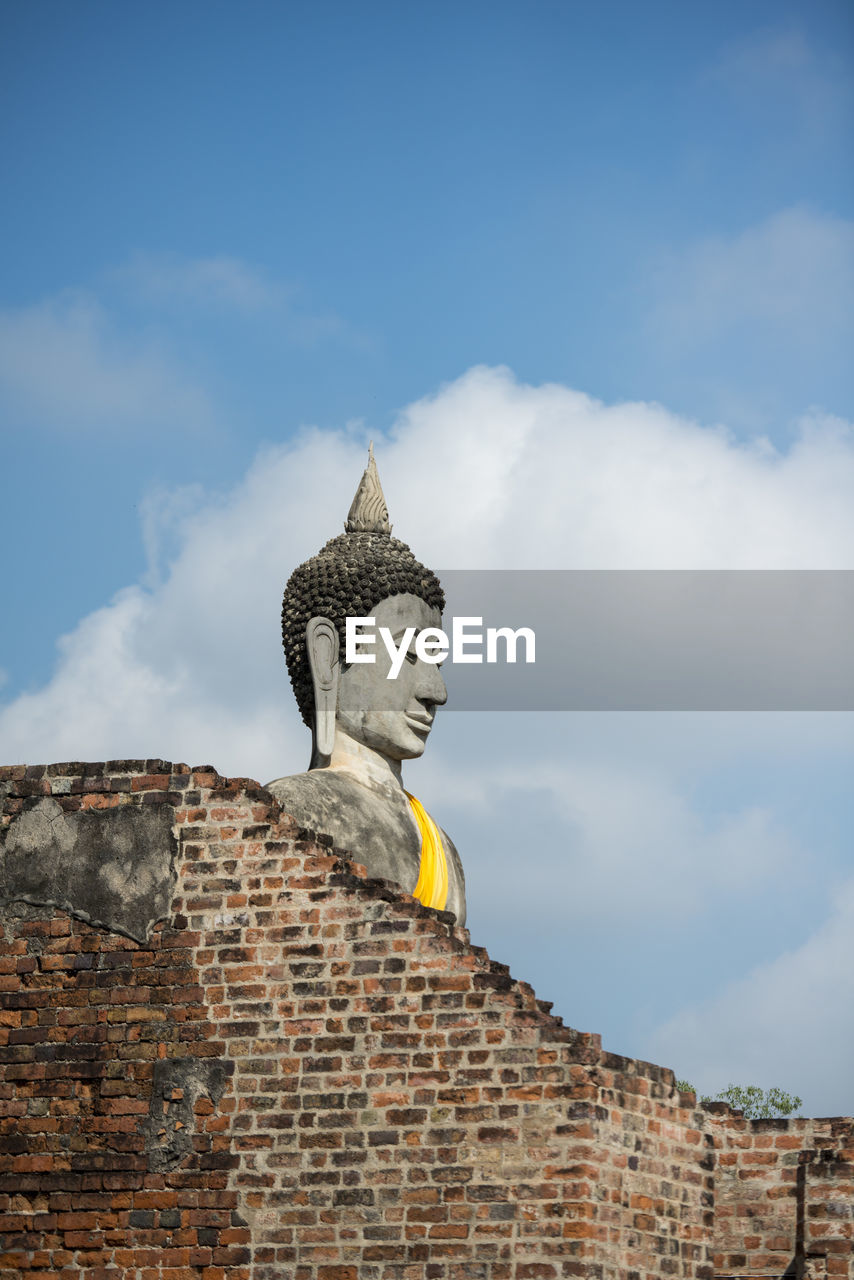 Low angle view of buddha statue by old brick wall at wat yai chai mongkhon