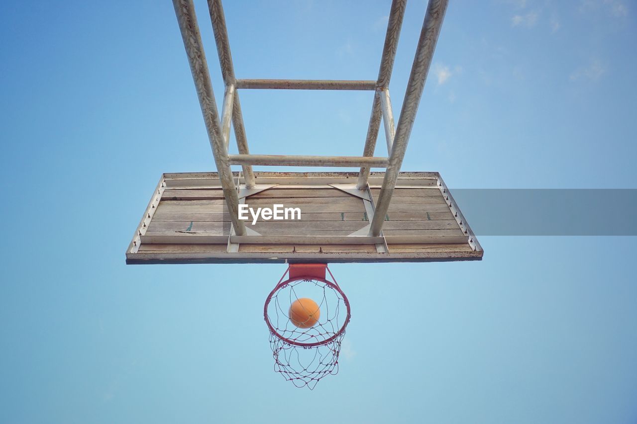 Low angle view of basketball falling into hoop against blue sky