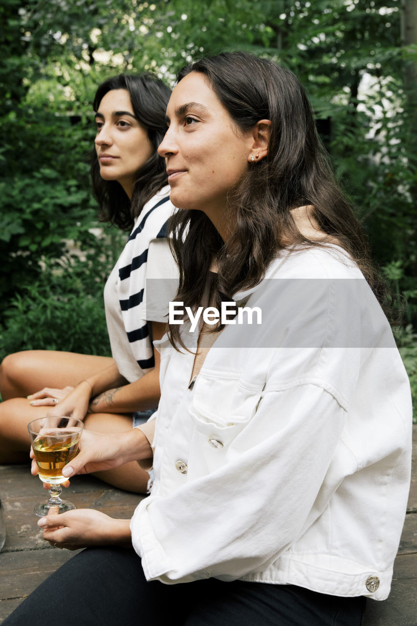 Smiling woman holding drink glass while sitting with female friend at party