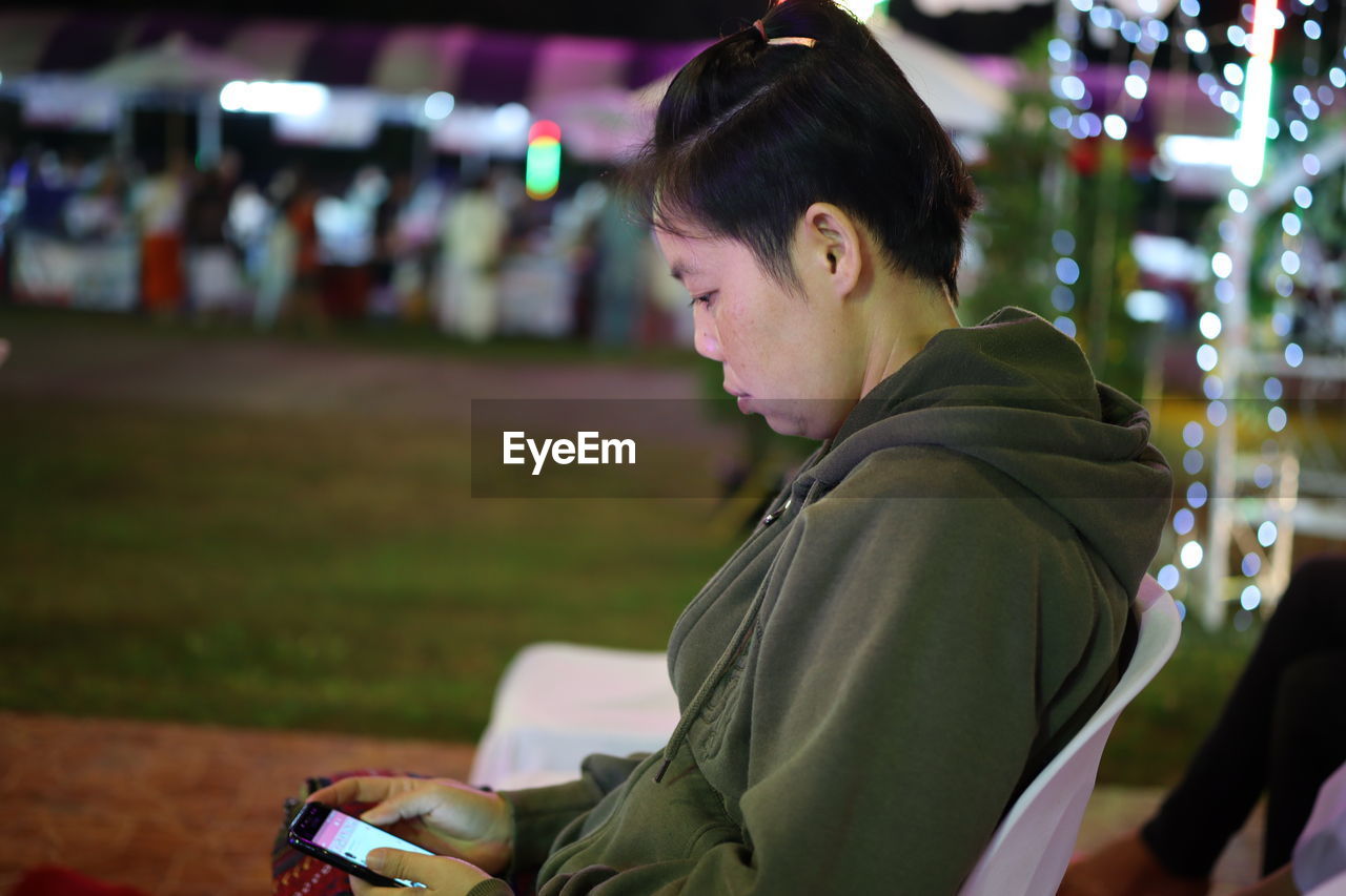 Side view of woman using smart phone while sitting on chair at night