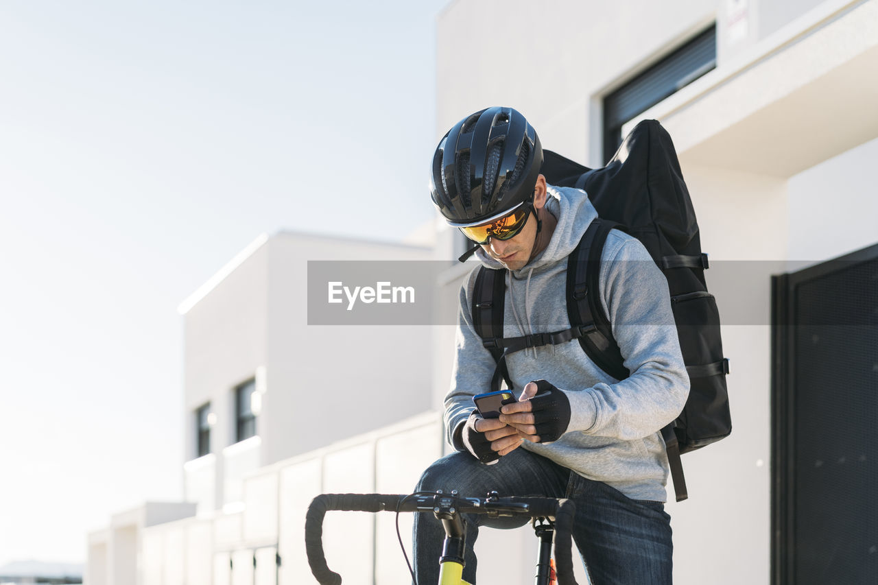 Delivery man with bicycle using smart phone on sunny day