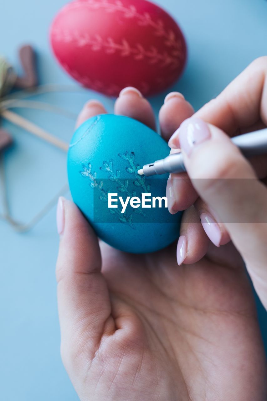 Cropped hands of woman drawing on blue easter egg