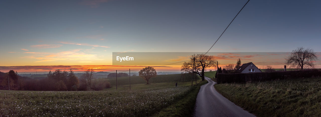 Road amidst field against sky during sunset