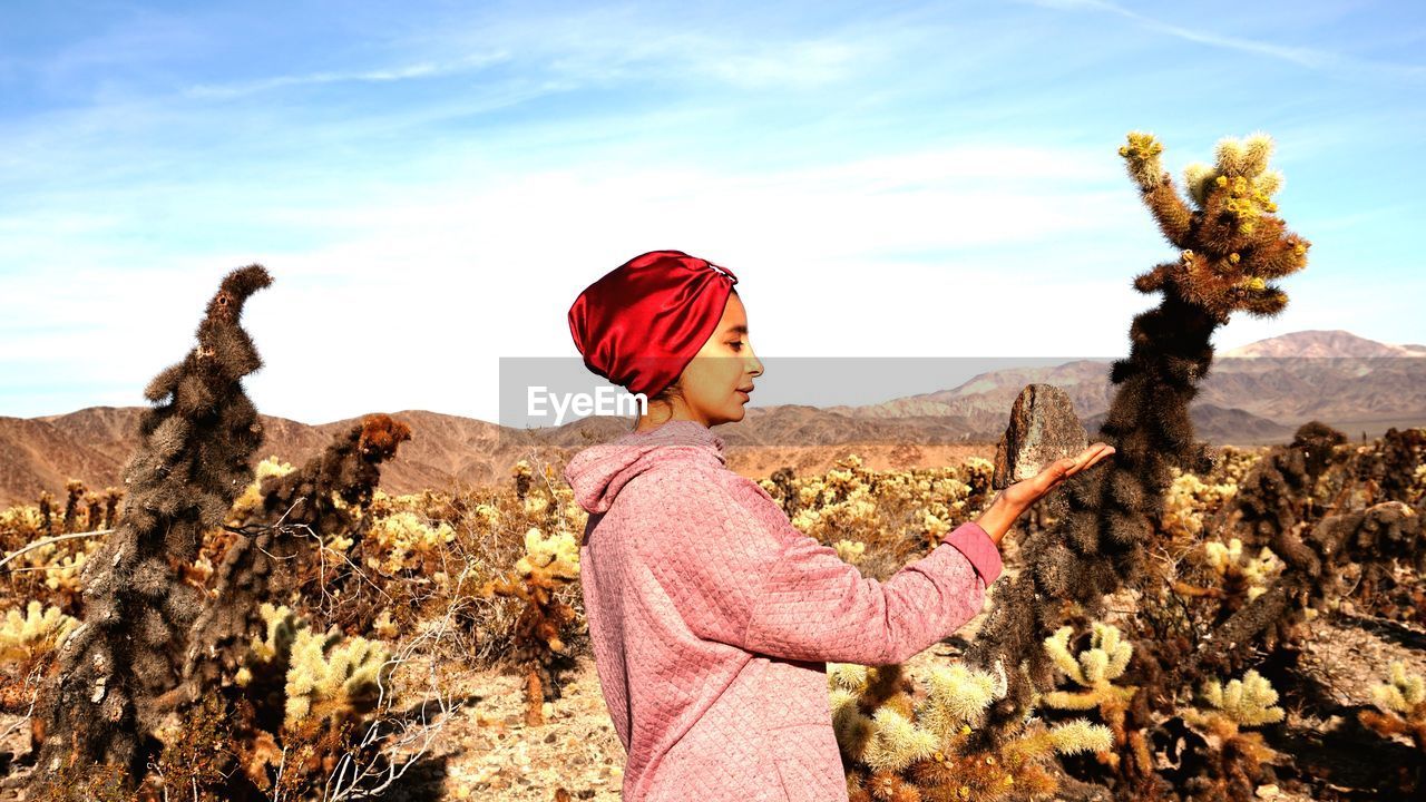 Side view of mid adult woman holding rock while standing against sky