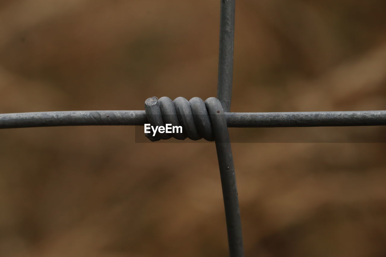 CLOSE-UP OF BARBED WIRE FENCE ON ROPE AGAINST BLURRED BACKGROUND