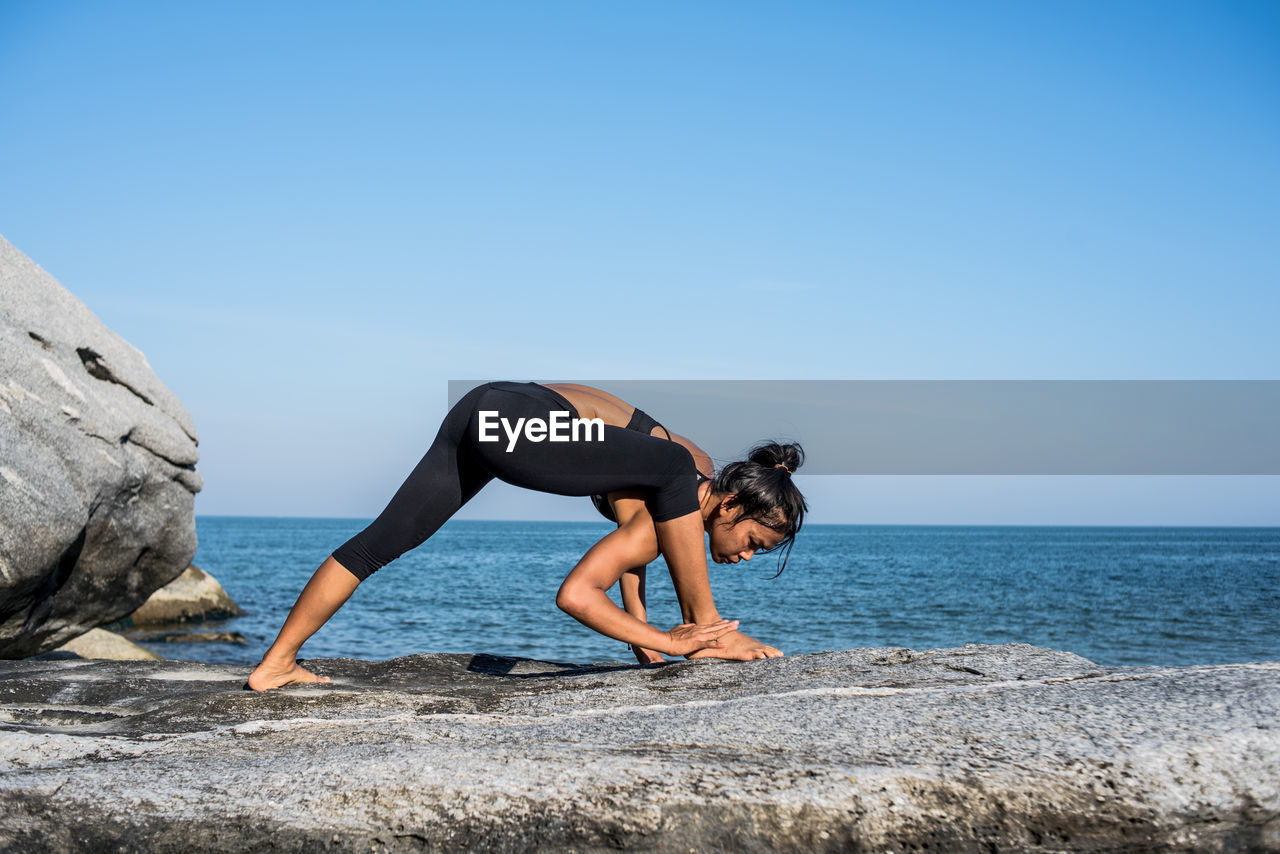 Young woman exercising at beach against sky