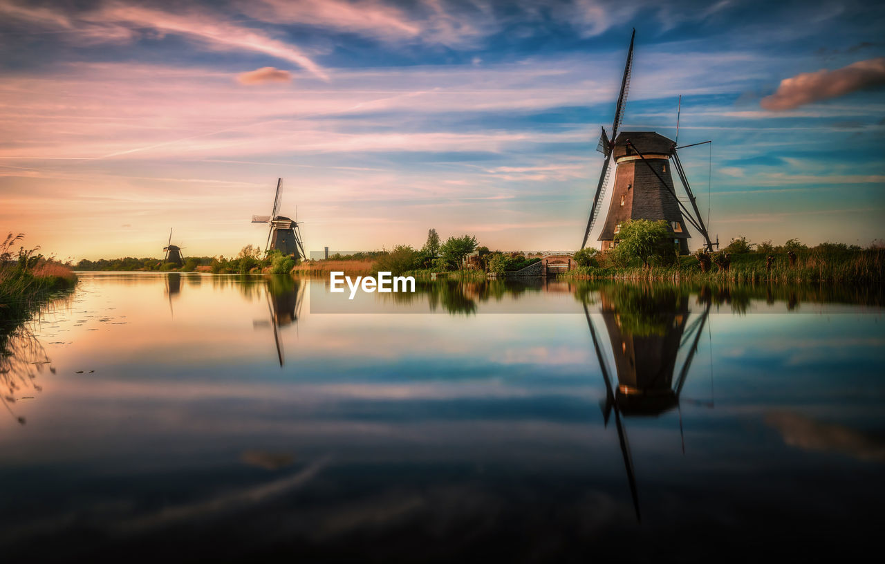 Reflection of traditional windmill in lake against sky during sunset