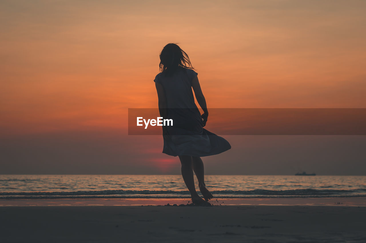 Woman standing at beach during sunset