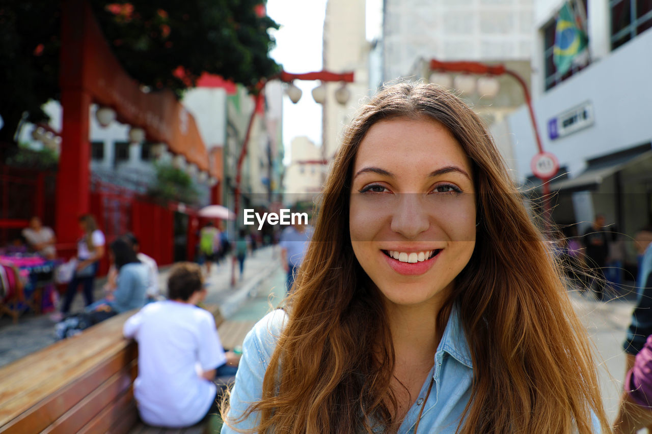 Portrait of smiling young woman against buildings in city