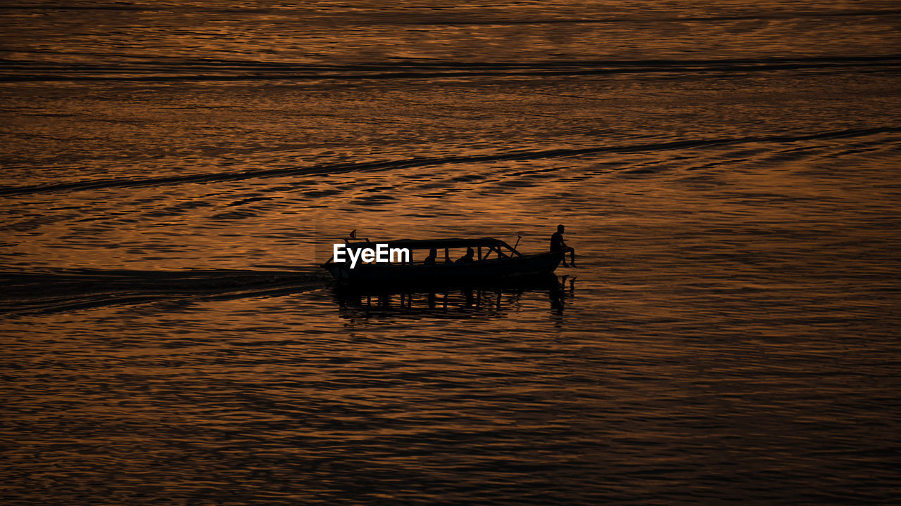 Silhouette person in boat on sea against sky during sunset