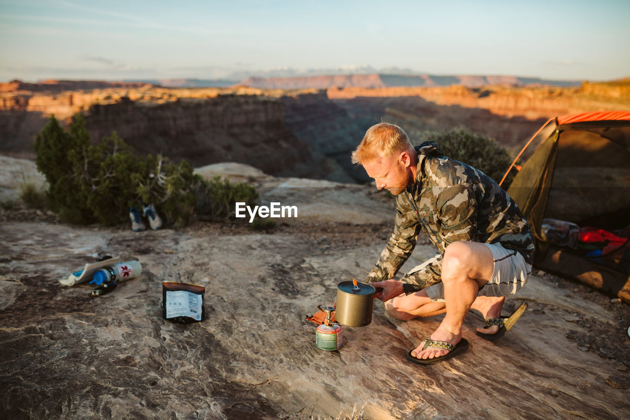 Male camper boils water with a whisper light at camp in desert